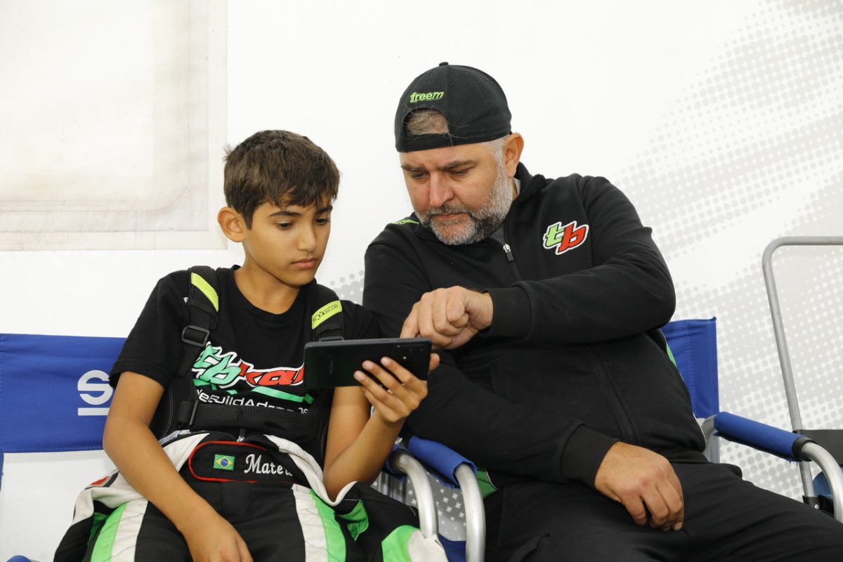 Young driver and his father from a Dutch youth karting team watching a race on a phone.